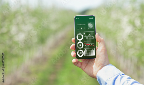 Farmer holding cellphone with smart gardening data on screen, monitoring soil ph, temperature, performing pest control