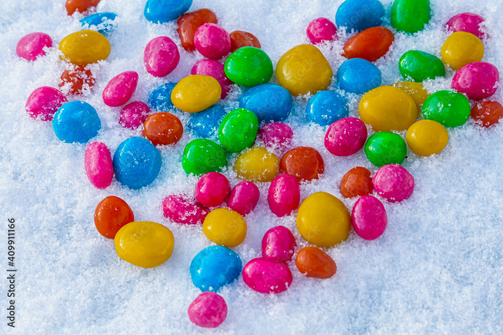 Multi-colored heart shaped candies in the snow. Sweets in the snow. Valentine's Day. Sweets as a gift. Romantic background for Valentine's Day. Multi-colored heart shaped candies in the snow. Sweets in the snow. Valentine's Day. Sweets as a gift. Romantic background for Valentine's Day.