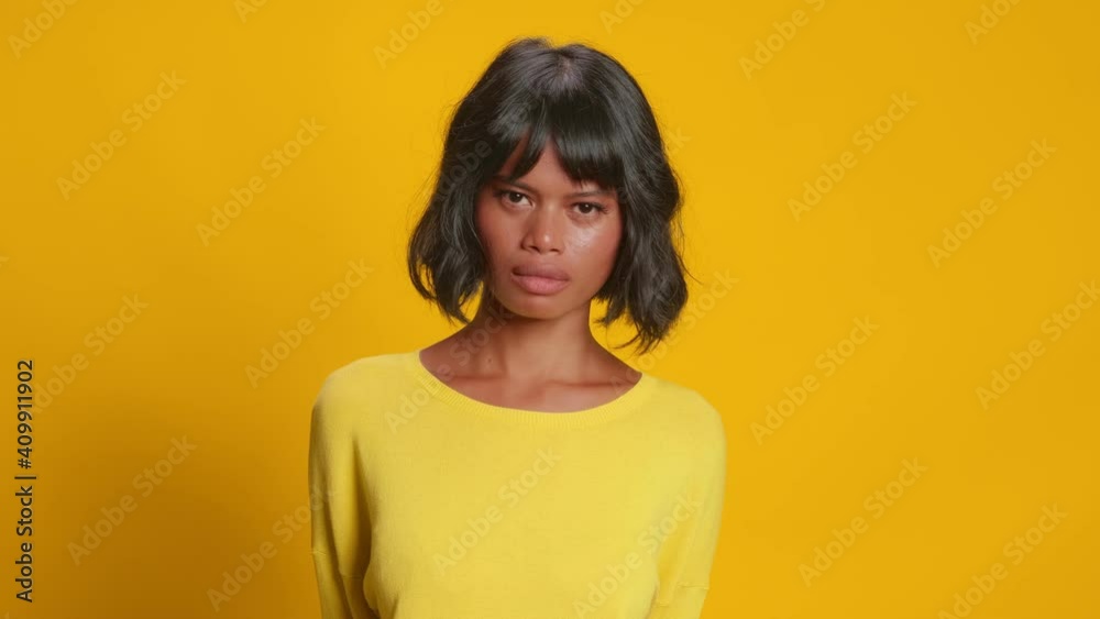 Serious young dark skinned woman shakes her head negatively making it clear that she does not agree. Female over yellow background disagrees and denies her involvement. Concept of human emotions.