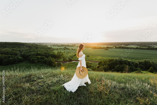 Young beautiful woman in boho style dress and hat on nature at sunset.