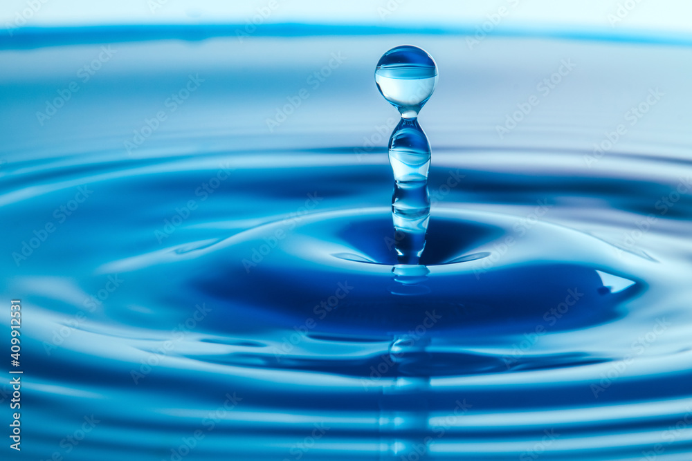 Dark blue water droplets splash close up on the water surface. It creates a water wave and a perfect crown Dark blue water droplets splash close up on the water surface. It creates a water wave and a perfect crown