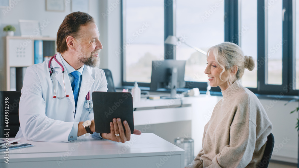 Friendly and Cheerful Family Doctor is Reading Medical History of Senior Female Patient During Consultation in a Health Clinic. Physician Using Tablet Computer in Hospital Office.