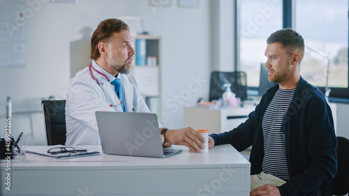 Senior Doctor is Prescribes Medicine in a Box to a Male Patient. Medical Consultation in a Health Clinic. Physician in White Lab Coat Sitting Behind a Computer in Hospital Office.  © Gorodenkoff