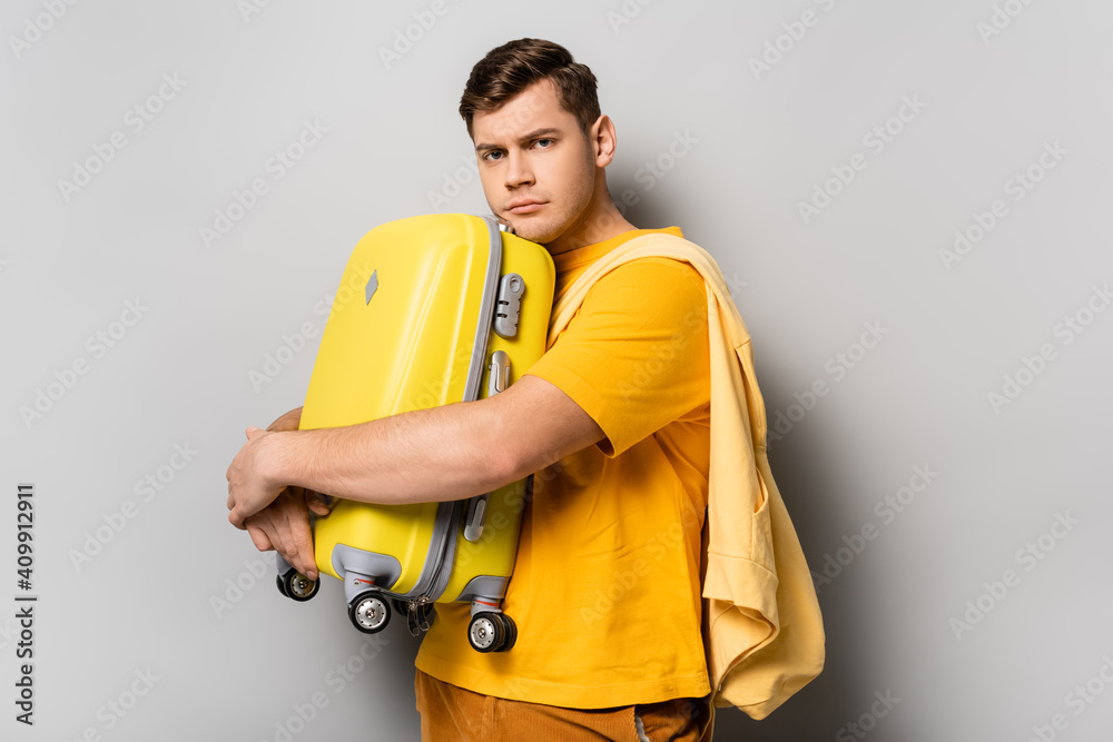 Upset traveler hugging suitcase on grey background Upset traveler hugging suitcase on grey background