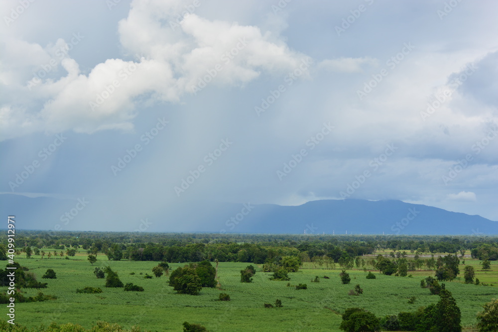 clouds over the mountains with raining in the front of it white and gray clouds and strong winds green farm land landscape in Thailand clouds over the mountains with raining in the front of it white and gray clouds and strong winds green farm land landscape in Thailand