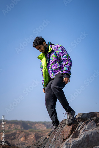 Young Indian boy standing on the top of cliff wearing a snow jacket and track pants. Enjoying and freedom concept.