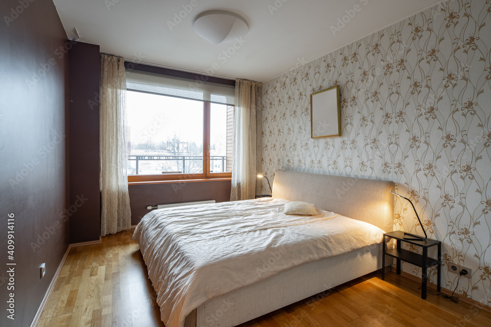 Contemporary interior of bedroom in modern flat. Cozy bed. Lamps on nightstands. Huge window. Hardwood floor. Contemporary interior of bedroom in modern flat. Cozy bed. Lamps on nightstands. Huge window. Hardwood floor.