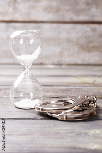 Serve sentence concept. Hourglass and handcuffs on wooden background.