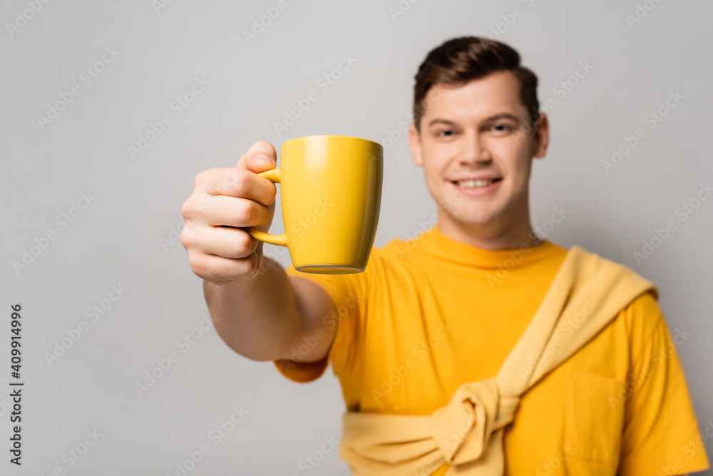 Yellow cup in hand of smiling man blurred on grey background Yellow cup in hand of smiling man blurred on grey background