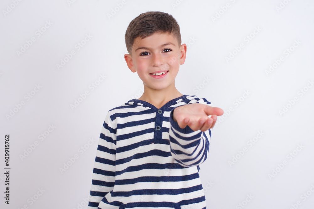 little cute boy kid wearing stripped t-shirt against white wall smiling friendly offering something with open hand or handshake as greeting and welcoming. Successful business. little cute boy kid wearing stripped t-shirt against white wall smiling friendly offering something with open hand or handshake as greeting and welcoming. Successful business.