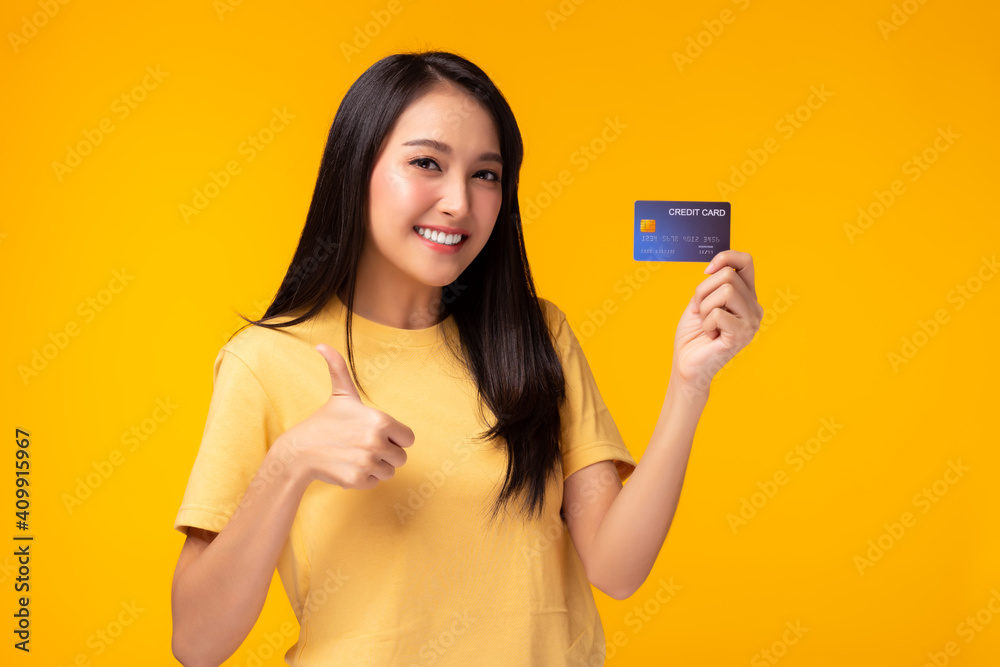 Young asian woman showing plastic credit card giving thumb up to credit card, standing over yellow background. Beautiful customer girl get satisfied of credit card service and promotion, smile face Young asian woman showing plastic credit card giving thumb up to credit card, standing over yellow background. Beautiful customer girl get satisfied of credit card service and promotion, smile face