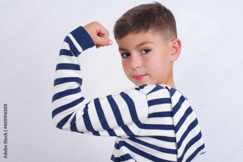 little cute boy kid wearing stripped t-shirt against white wall, showing muscles after workout. Health and strength concept. little cute boy kid wearing stripped t-shirt against white wall, showing muscles after workout. Health and strength concept.