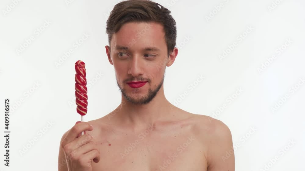 Confident transvestite half naked brunette bearded man hold sweet lollipop, look camera, awkwardly hints for date, flirt, smile isolated on white background. Single beautiful male with women cosmetic.