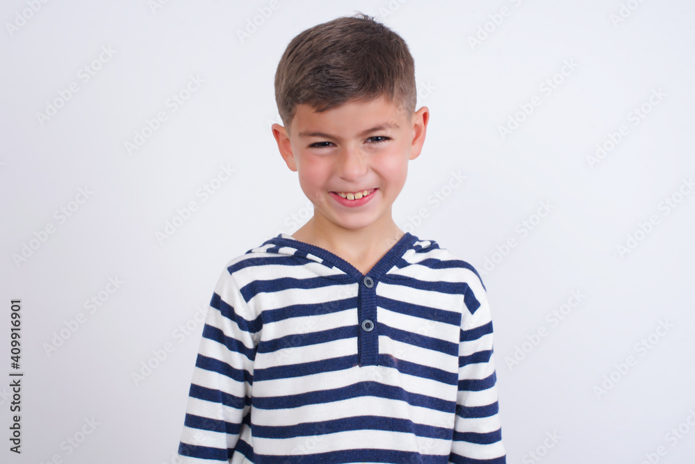 Mad crazy little cute boy kid wearing red stripped t-shirt against white wall clenches teeth angrily, being annoyed with coming noise. Negative feeling concept. Mad crazy little cute boy kid wearing red stripped t-shirt against white wall clenches teeth angrily, being annoyed with coming noise. Negative feeling concept.
