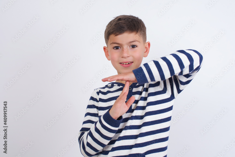 little cute boy kid wearing red stripped t-shirt against white wall feels tired and bored, making a timeout gesture, needs to stop because of work stress, time concept.