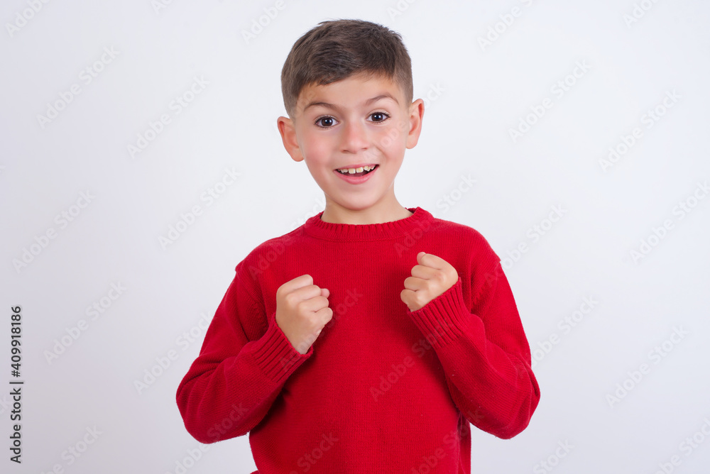 Portrait of desperate and shocked Little cute boy kid wearing red knitted sweater against white wall looking panic, holding hands near face, with mouth wide open. Portrait of desperate and shocked Little cute boy kid wearing red knitted sweater against white wall looking panic, holding hands near face, with mouth wide open.