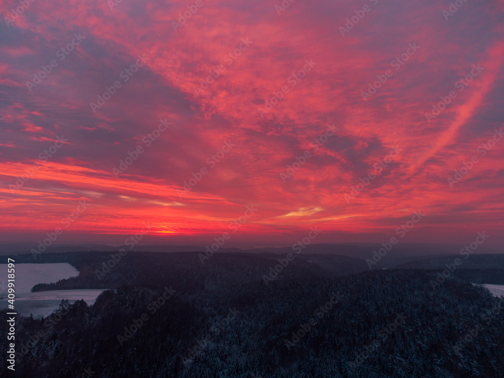 Drone panorama of amazing red sunrise behind clouds over bavarian forest and field area with snow in winter