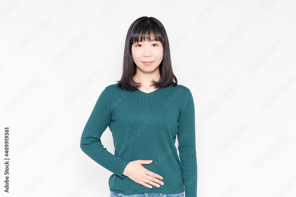 白背景の前に立って、お腹に手を当てている女性