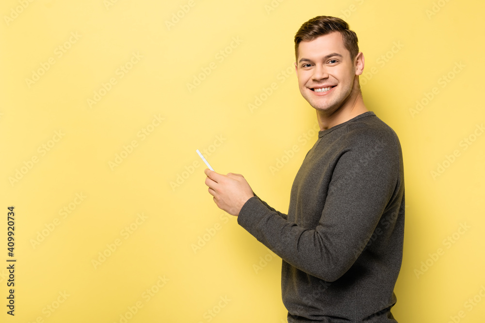 Smiling man using mobile phone and looking at camera on yellow background Smiling man using mobile phone and looking at camera on yellow background