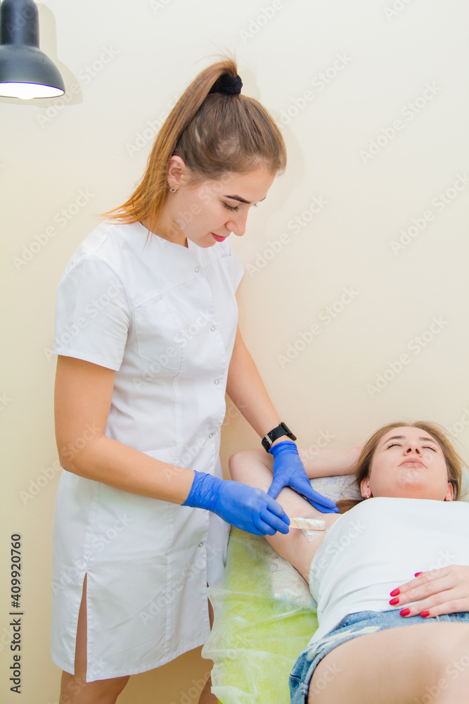 Young woman in a white coat, an epilation specialist at work in a beauty salon.