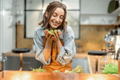 Portrait of pretty woman in apron with fresh brussels sprouts on the kitchen at home. Healthy cooking concept. High quality photo