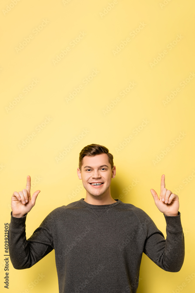 Man pointing with fingers and smiling at camera on yellow background Man pointing with fingers and smiling at camera on yellow background