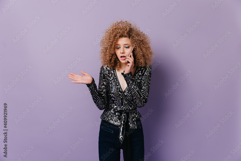Serious lady in black blouse with silver beads is talking on telephone. Snapshot of young woman with blond curly hair Serious lady in black blouse with silver beads is talking on telephone. Snapshot of young woman with blond curly hair
