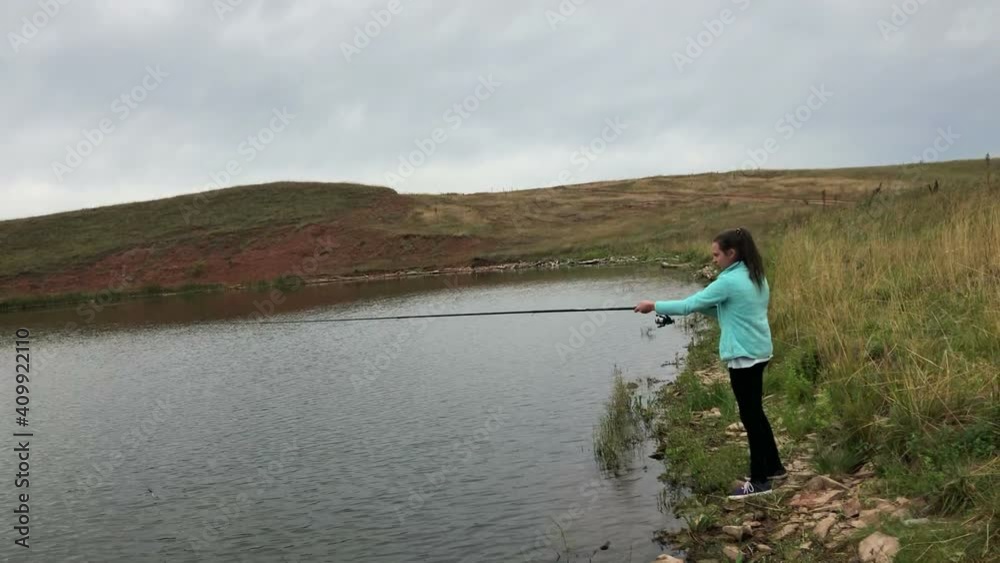 Teen age Caucasian girl cast the fishing rod while standing on lake shore. Recreational fishing in freshwater pond Teen age Caucasian girl cast the fishing rod while standing on lake shore. Recreational fishing in freshwater pond