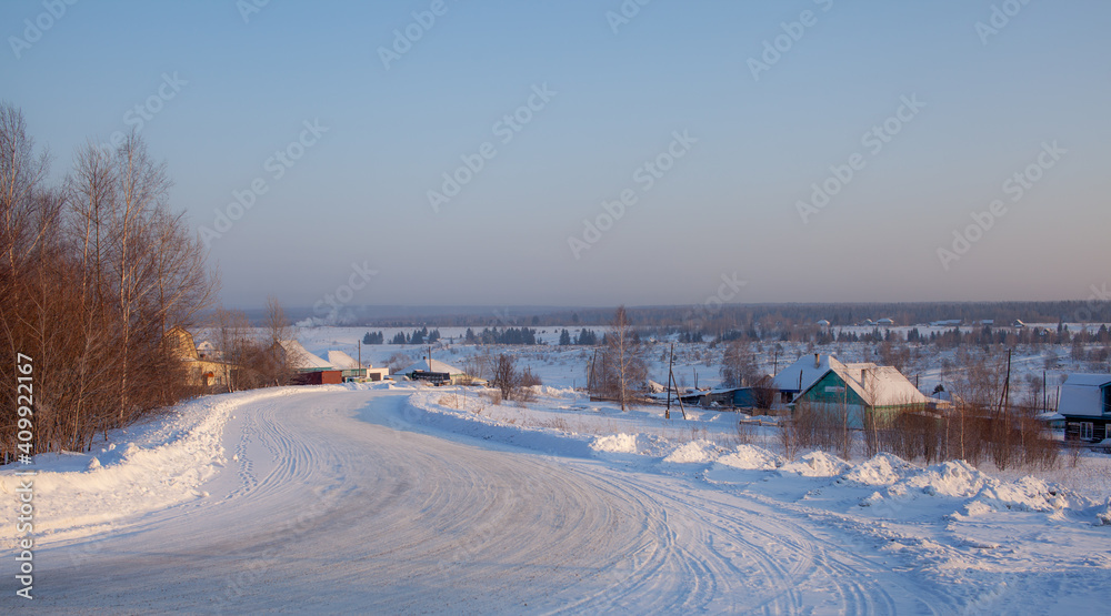 A snow-covered village with houses and a vered road leading to it.