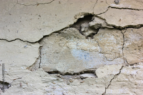 Cracks in the facade of an old clay house. Time-damaged wall of historic Ukrainian-style house. Backgrounds and textures of a beige wall