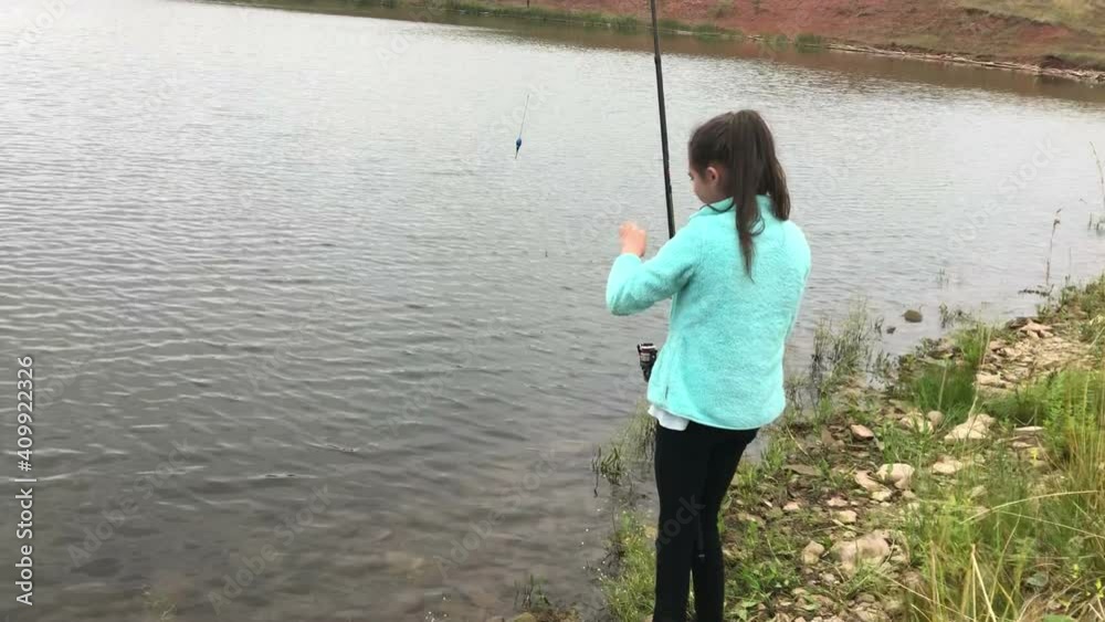 Teenage girl catching fish with rod on lake shore. Recreational fishing in freshwater pond Teenage girl catching fish with rod on lake shore. Recreational fishing in freshwater pond
