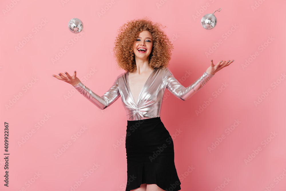 Girl in great mood juggles with mini disco balls. Portrait of curly lady in shiny blouse on pink background Girl in great mood juggles with mini disco balls. Portrait of curly lady in shiny blouse on pink background