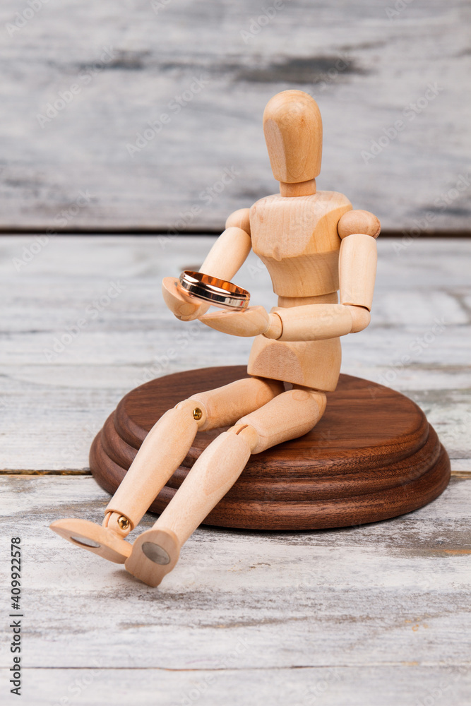 Miniature wooden mannequin with wedding ring. Sitting dummy holding golden ring vertical shot. Miniature wooden mannequin with wedding ring. Sitting dummy holding golden ring vertical shot.