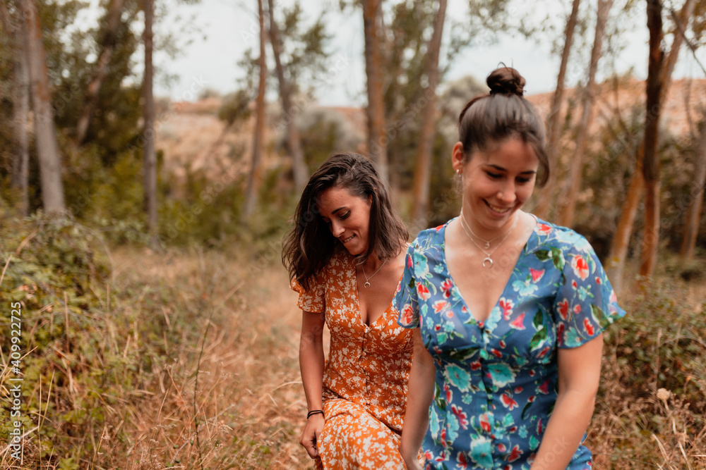 Fototapeta premium Two young lesbians walking in the woods wearing long dresses