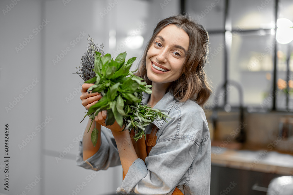 Portrait of cheerful woman in apron with fresh spicy herbs basil, rosemary, thyme on the kitchen. Healthy cooking concept. High quality photo