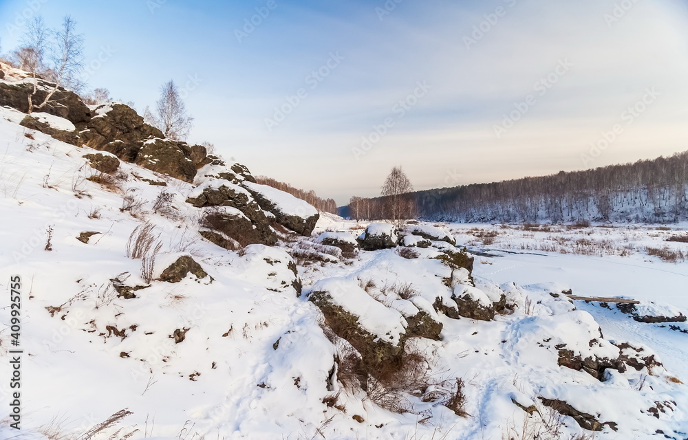 Winter landscape with frozen river, snow, rocks and trees