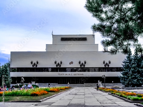 The building of the Sumy Regional Drama and Music Comedy Theatre named after M. Shchepkin in the evening (Ukraine). Modern building in city square with flowerbeds and people photo
