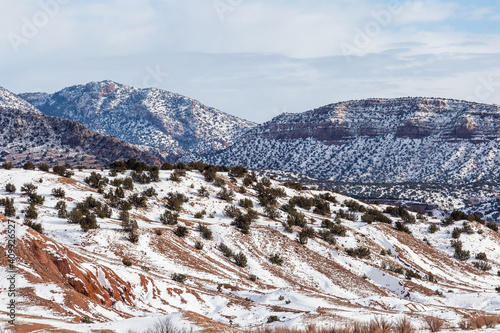Snow covered mountain range with green brush and red rocks on cloudy day in rural New Mexico