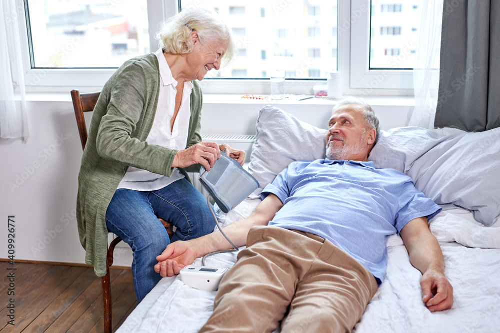 mature male patient at hospital with worried wife sitting with him, while checking blood pressure with tonometer. woman helps, support mature male patient at hospital with worried wife sitting with him, while checking blood pressure with tonometer. woman helps, support