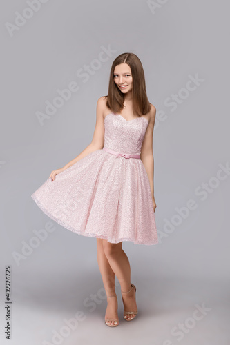 Young beautiful girl in a pink dress stands on a gray background