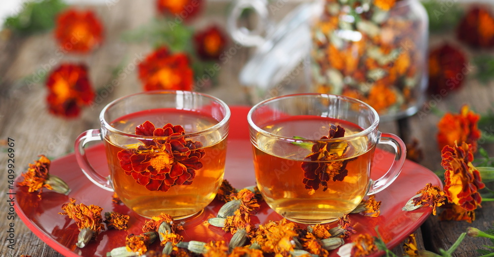 Autumn healing background. Tea cups with herbal tea with calendula flowers or Chernobrivtsi or Mary's Gold on a red plate on a vintage wooden background with dried flowers. Autumn healing background. Tea cups with herbal tea with calendula flowers or Chernobrivtsi or Mary's Gold on a red plate on a vintage wooden background with dried flowers.
