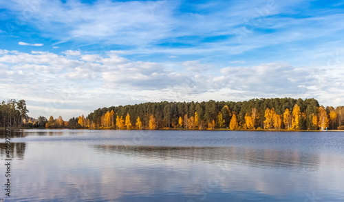 Lake view, yellow and green trees, blue sky with white clouds in autumn