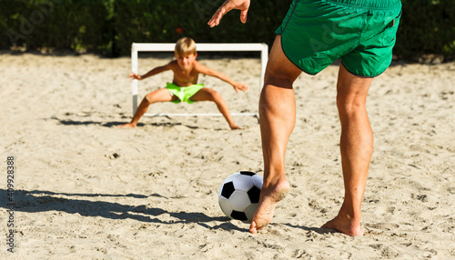 Dad has fun with his son playing with a soccer ball at the beach, in the summer on a sunny day. photo