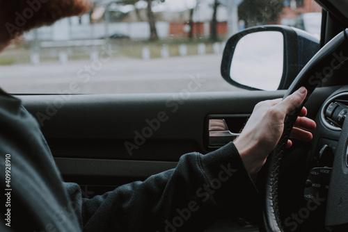 Detalle de un conductor joven en un coche con las manos en el volante. Se ve el espejo retrovisor del automóvil