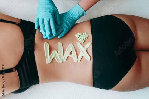 Top view on inscription wax laid out with hot wax for depilation. Hair removal procedure on female back. Heart which composed of granules of depilatory wax. The gloved hands of the depilation master.