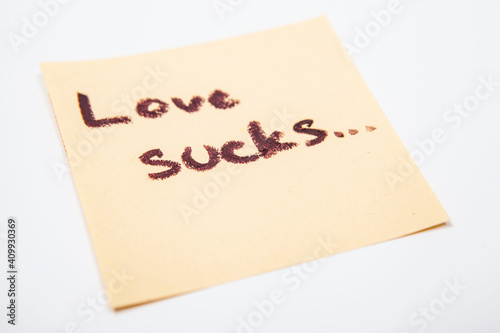 Close up of love sucks note handwritten on yellow sticky paper