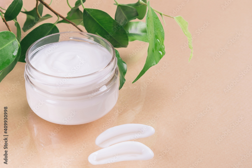 Jar with cosmetic cream and green leaves on beige background. Skincare, facial moisturizing, natural organic cosmetics concept. Copy space, close up Jar with cosmetic cream and green leaves on beige background. Skincare, facial moisturizing, natural organic cosmetics concept. Copy space, close up