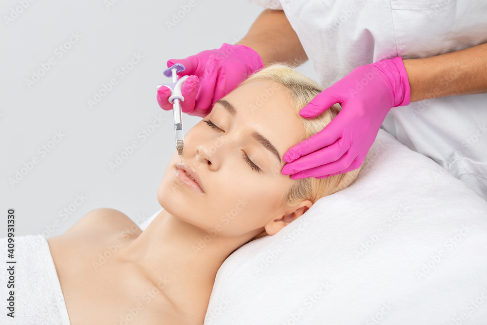 Naklejka premium Cosmetologist does injections for lips augmentation and anti wrinkle in the nasolabial folds of a beautiful woman. Women's cosmetology in the beauty salon.