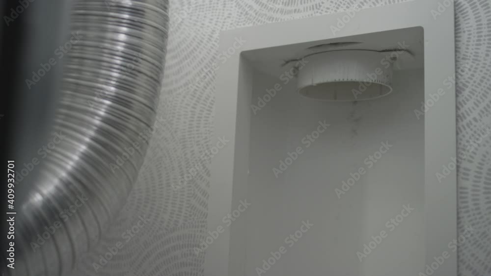 Woman disconnects the dryer vent hose from the wall