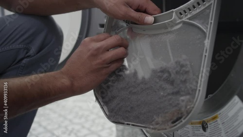 Man pulls out the lint trap from a clothes dryer and pulls the lint off photo